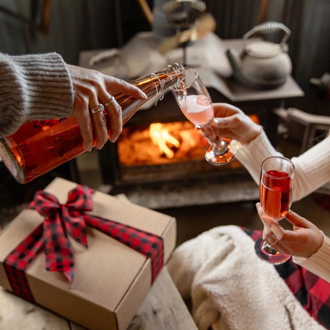 Couple célébrant la st-valentin au coin du feu en dégustant un cidre de pommes et griottes sans alcool de Labonté de la Pomme, vendu chez Bocaux et co. à Ste-Marthe-sur-le-Lac